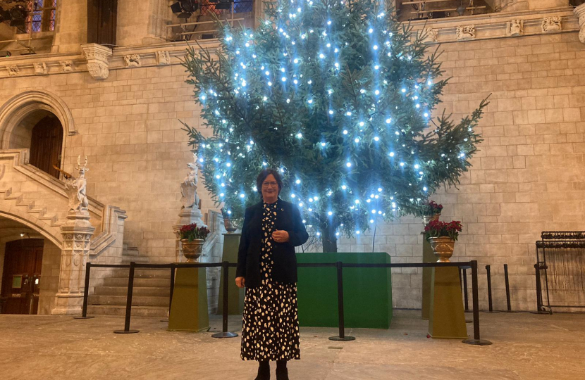 Pauline Latham OBE MP stands in front of a Christmas Tree